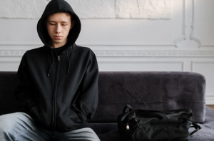Teenage boy in black hoodie sitting on couch looking sad