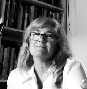 Black-and-white photo of a woman in a blouse and glasses smiling in front of a bookcase.