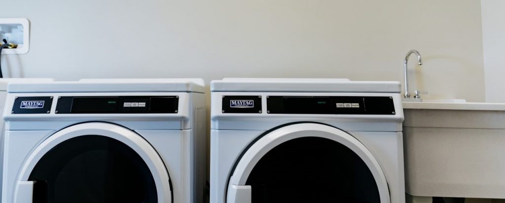 Two washing machines, side by side, next to a deep laundry sink.