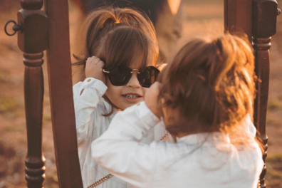 a little girl wearing adult sun glasses and looking at herself in a mirror