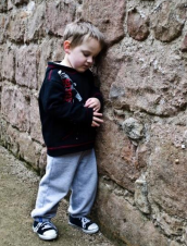 a young child leaning up against a stone wall and looking down at the ground