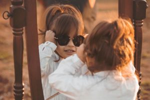 A child looking at herself wearing glasses in a mirror.