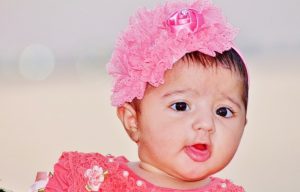 A female infant wearing stereotypically feminine clothing and accessories.
