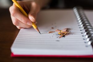 Photo of a person writing with a pencil in a notebook.