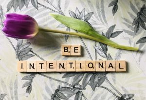 The word "Be Intentional" on a table with a flower