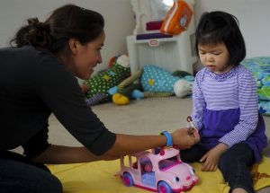 Young girl sitting on the floor with an adult and a toy car
