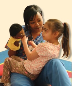 Teaching holding a young girl and a puppet on her lap