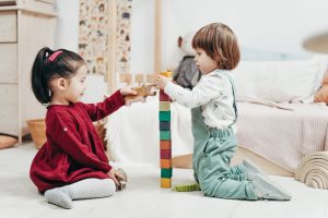 Two young girls building a block tower together