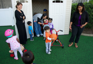 Three teachers and five children playing in the backyard with balls and riding toys