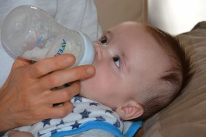 Infant drinking from a bottle in caregiver's arms