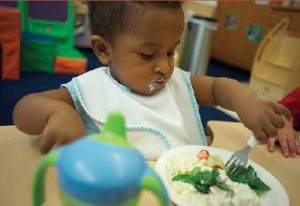 Young boy feeding himself with a small fork and sippy cup
