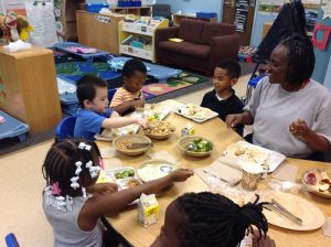 Caregiver sitting and eating with six children