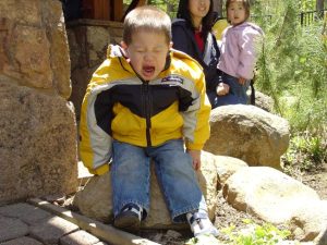 Young boy sitting on a rock and crying while a caregiver and your girl look on