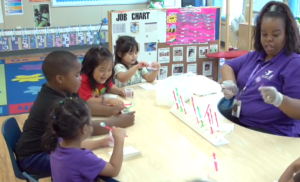 Four children sitting at table and practicing teeth brushing with their teacher.