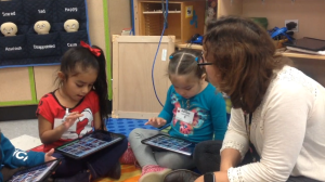 These children and their teacher in a bilingual preschool classroom are using an app to create a “story” with photos of their recent field trip.