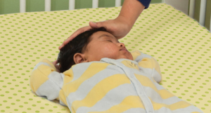 baby sleeping in a crib on their back, caregiver's hand patting their head