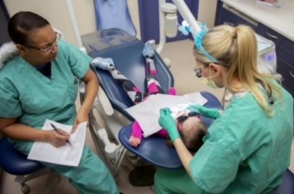 Dentist and assistant checking a child for dental caries (cavities).