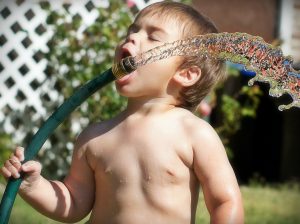 Child drinking water from a garden hose.