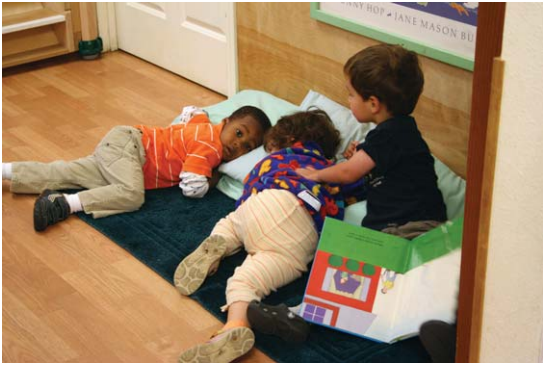 Three young children lay in a nap area, they are awake.