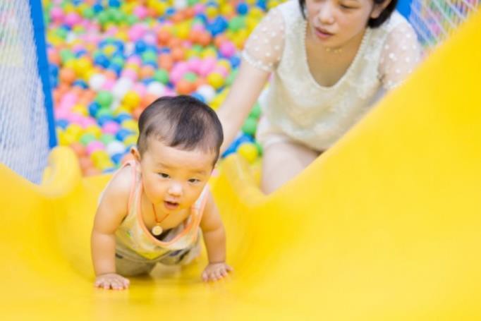 Adult supervising an infant crawling up a slide.