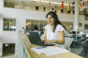 student smiling while using laptop on campus