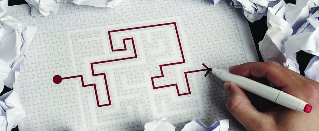 A hand is holding a red marker and solving a maze puzzle in red ink.