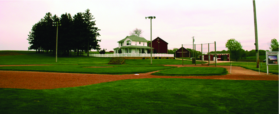 An empty baseball diamond with a farmhouse in the background.