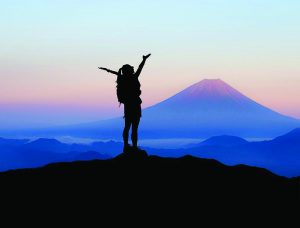 A silhouetted mountain climber standing at a peak, arms outstretched to the sky.