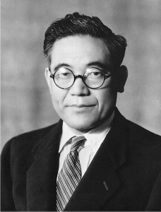 A black and white photo of a man in a suit wearing glasses.