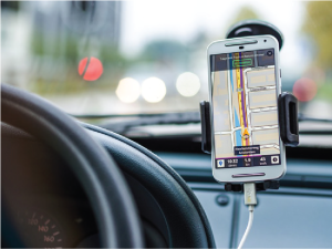 A smartphone mounted next to a car's steering wheel displays a map.