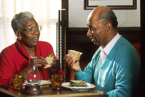 An African American man and woman eating lunch at a small restaurant table.