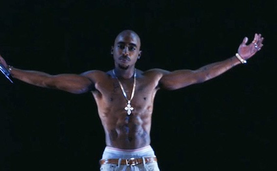 Image of "holographic" Tupac facing the camera, shirtless, holding microphone and with arms outspread.