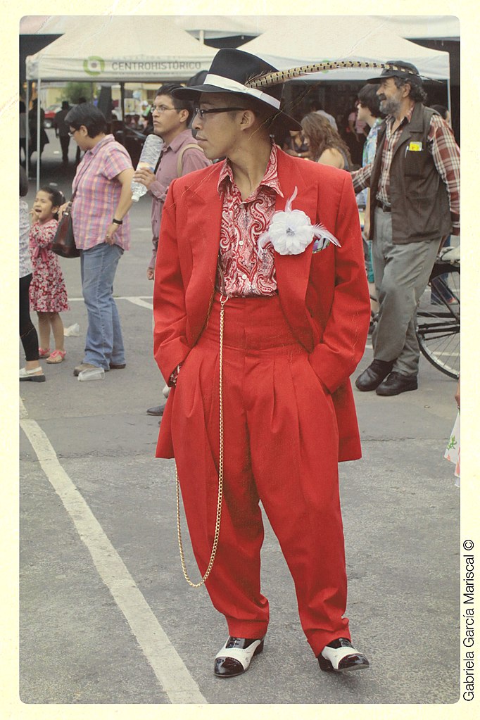 Man in city street wearing a flamboyent red zoot suit and hat with a peacock feather.