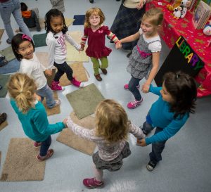 Kindergarten girls at the library hold hands while dancing in a circle