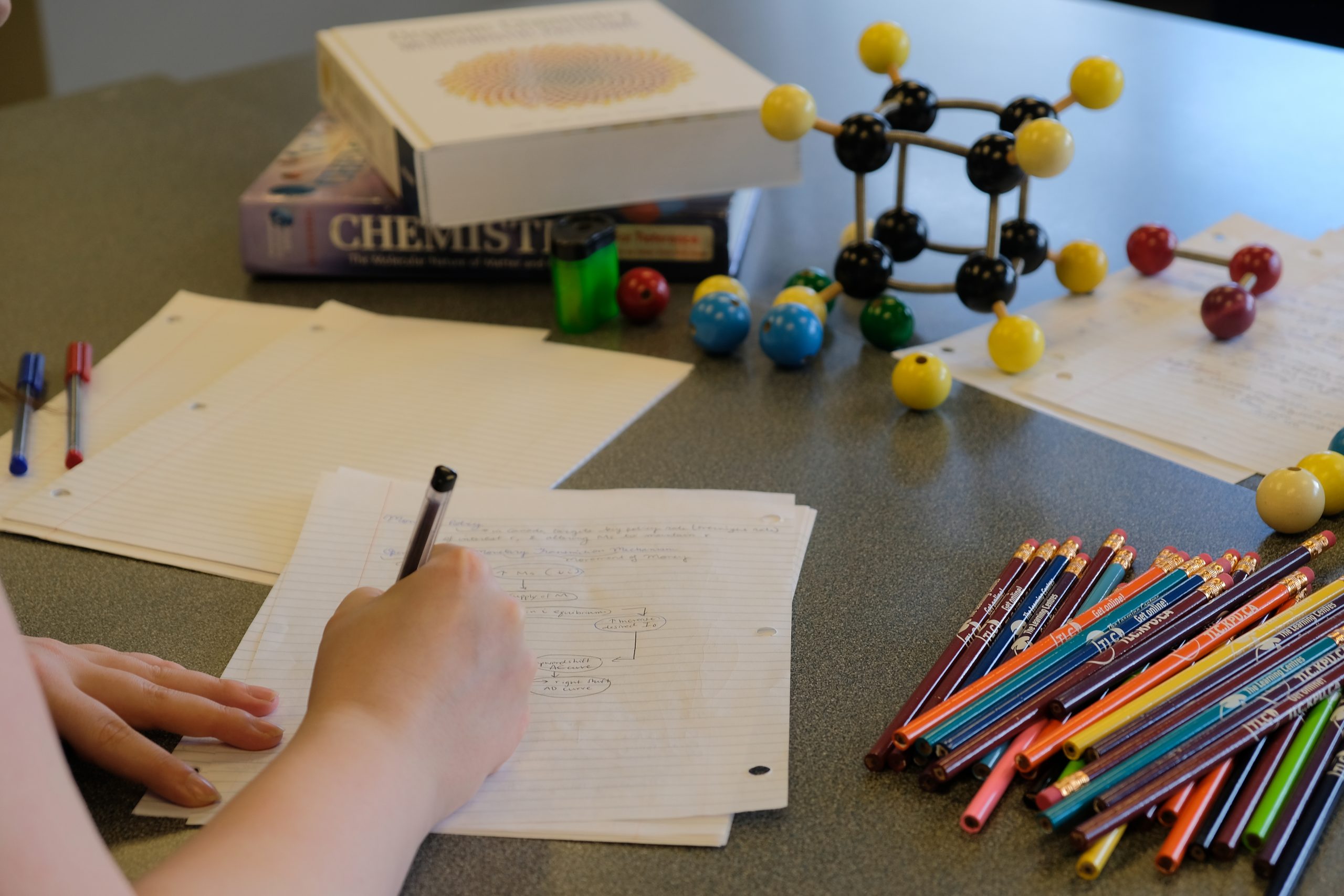 Student taking notes with pencils and chemistry models