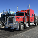 The image shows a large, red semi-truck with a long, flat trailer attached