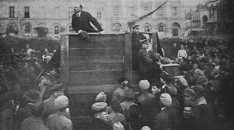 Lenin standing on a platform giving a speech to a crowd.
