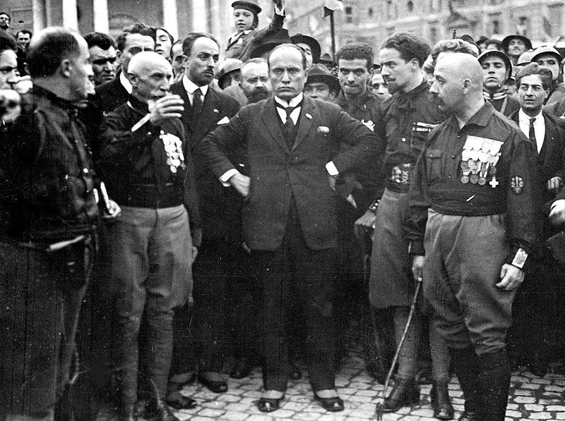 Mussolini standing in the midst of blackshirt Fascists.