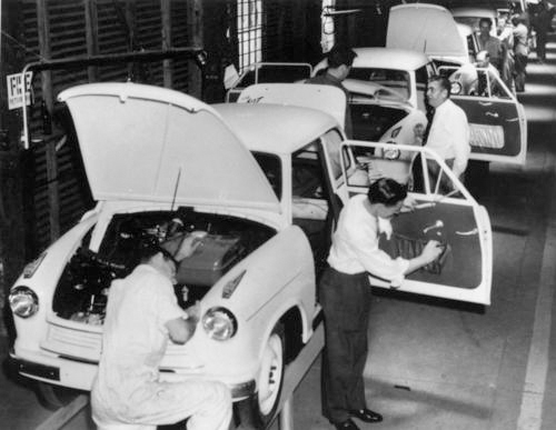 A black and white photo of people working on a car assembly-line.