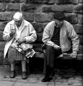 Two older people sitting on a street bench not looking at each other.