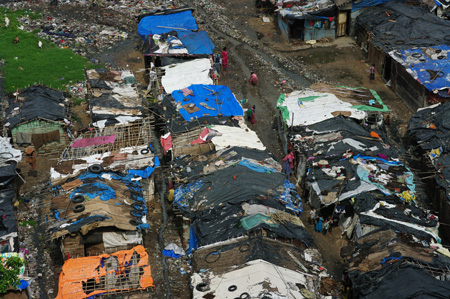 Dilapidated slum dwellings with tarps weighed down with tires used as roofs.