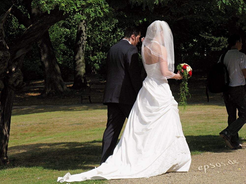 A bride and groom holding hands walking through a park.