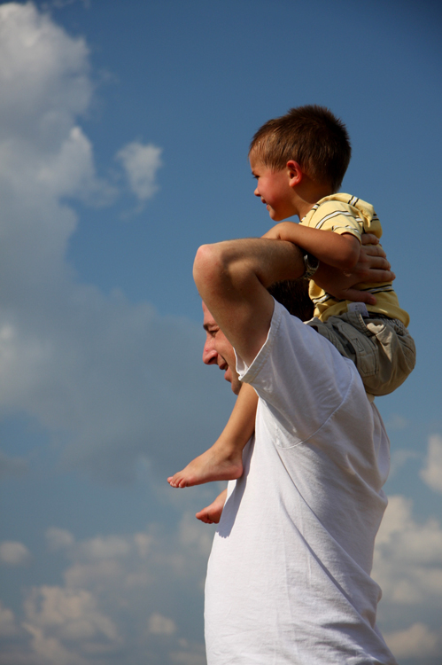 A young boy sits on the shoulders of a man who holds him in place.
