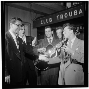 Black and white photo of young men in suits. Two of the men hold musical instruments.