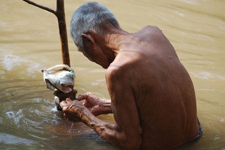 An old man standing in a lake or river. He appears to be fixing something.