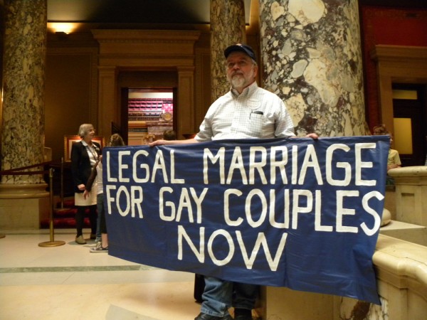 A man holding a sign that says, "Legal marriage for gay couples now."