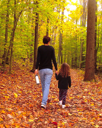 A woman walks through a forest holding the hand of a young girl.