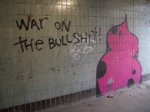 A spray paint on a wall saying "war on the bullshit" next to a pink stool