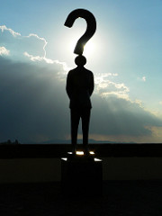 Silhouette of a man as the dot in the question mark standing in front of the sun.