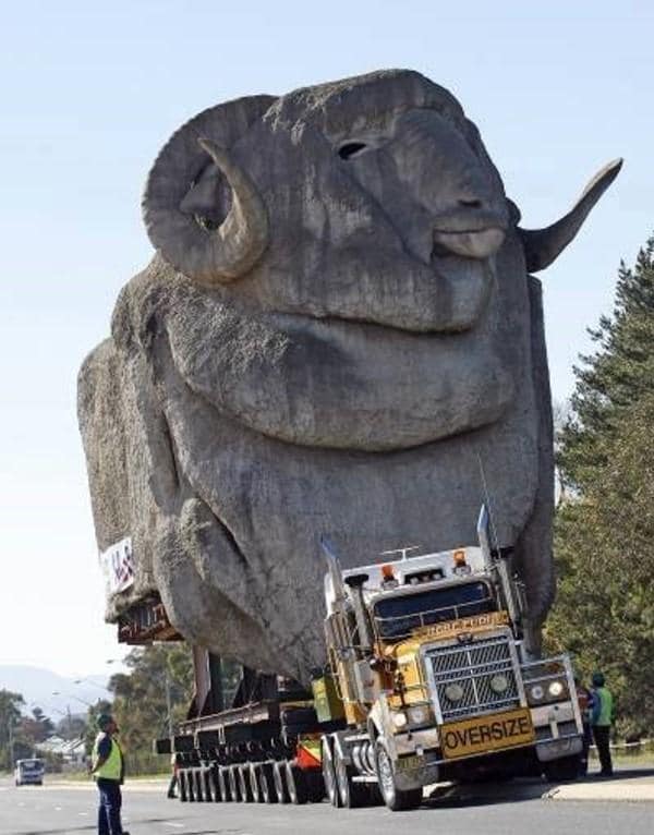 A photograph depicting a large stone ram on top of a semi-truck with the “OVER-SIZE” label on its front bumper. The ram appears to be more than three times the height of the semi-truck.